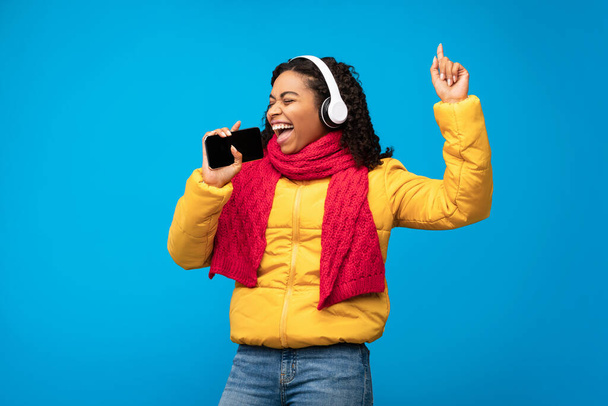 Ευτυχισμένο μαύρο κορίτσι σε ακουστικά τραγούδι σε μπλε φόντο - Φωτογραφία, εικόνα
