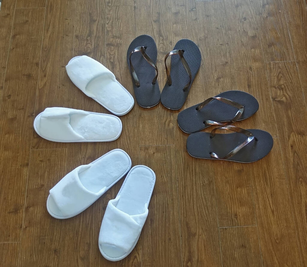   Four pairs of slippers, soft white and plastic brown, are on the floor. Shoes are arranged in a circle like flower petals.                              - Photo, Image