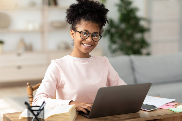 Dizüstü bilgisayardaki siyah genç kız internette evde oturuyor. - Fotoğraf, Görsel