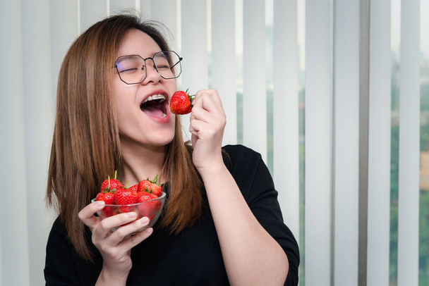 Ασιάτισσα όμορφη γυναίκα κρατώντας και τρώγοντας φρέσκια φράουλα είναι κόκκινο μούρο χρώμα φρούτων και γλυκό ζουμερό με απολαύσετε και χαρούμενη συγκίνηση στην έννοια των τροφίμων, υγιεινό φαγητό στη ζωή - Φωτογραφία, εικόνα