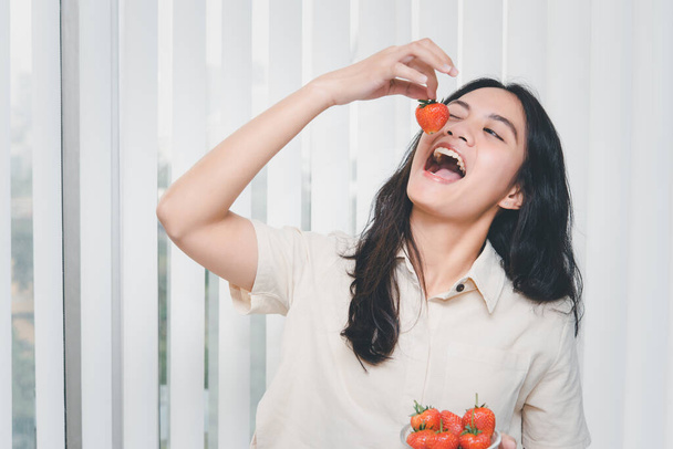 Mulher bonita asiática segurando e comendo morango fresco é cor de fruta de baga vermelha e doce suculento com prazer e emoção feliz na comida conceito, alimentação saudável na vida - Foto, Imagem