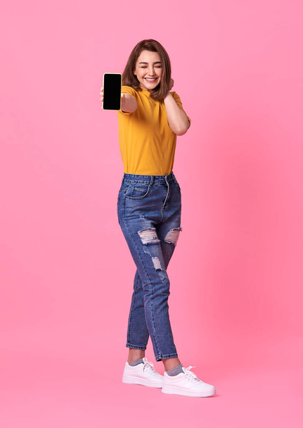 Portré boldog fiatal nő mutatja az üres képernyőn mobiltelefon elszigetelt rózsaszín háttér. - Fotó, kép