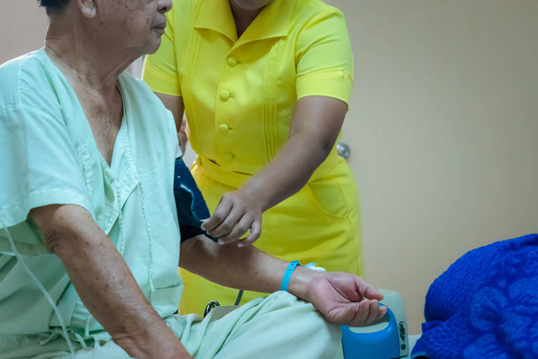 Pacient asijské starší muž 70s chřipka covid19 zdravotní kontrola podle tlakoměru na starší pacientské rameno na lůžku pacienta na jednotce intenzivní péče (JIP.) pokoj v nemocnici v konceptu zdravotní péče v životě - Fotografie, Obrázek