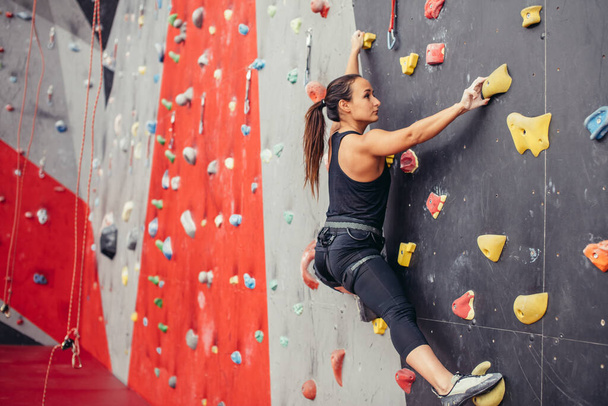 Young climber woman climbing on practical rock in climbing center, bouldering - Фото, изображение