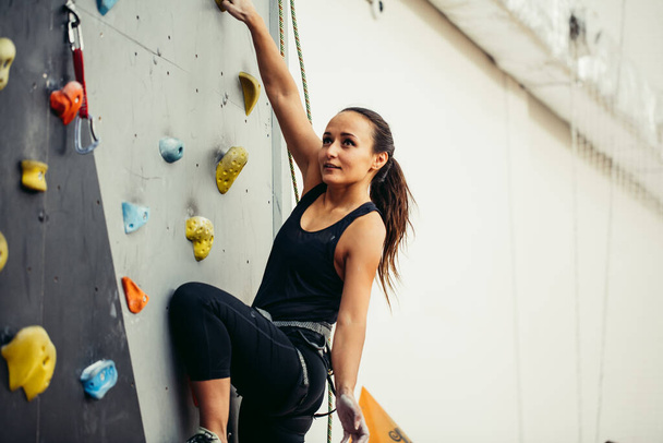 Woman practicing rock climbing on artificial wall indoors. Active lifestyle and bouldering concept. - Foto, Imagem