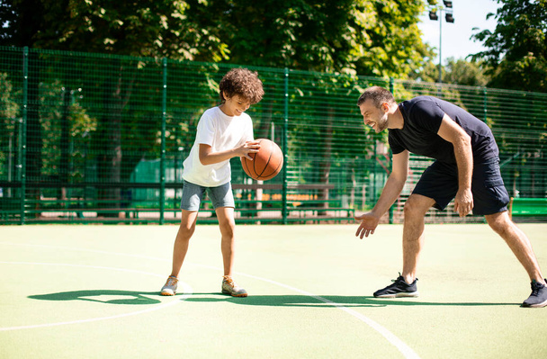 Maduro entrenador enseñando chico cómo jugar al baloncesto - Foto, Imagen