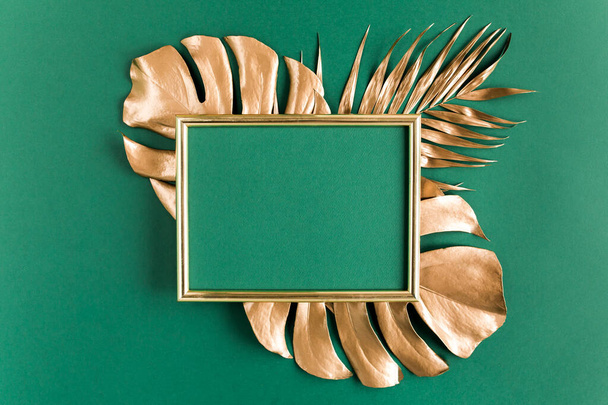 Gold tropical palm leaves Monstera and photo frame on green background. Flat lay, top view minimal concept. - Фото, зображення