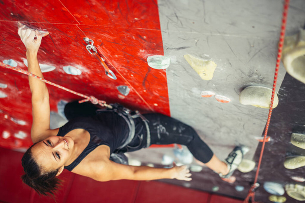 Beautiful young strong woman climbing on red artificial wall top view. - Fotó, kép
