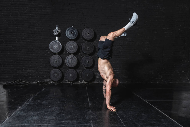 młody silny dopasowanie muskularny człowiek robi ręka stać i chodzić w siłowni jako hardcore cross trening - Zdjęcie, obraz