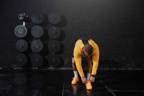 Young muscular fit man in sportswear ties a shoelace before hardcore cross workout and training in the gym - Foto, imagen