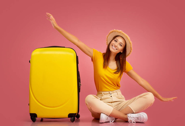 Chica emocionada sentada junto a la maleta, imitando el avión - Foto, imagen