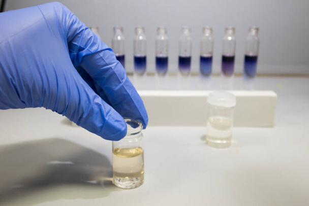 Test dell'olio di cannabis in laboratorio. Scienziato con una mano guantata che analizza una fiala di olio di CBD - Foto, immagini