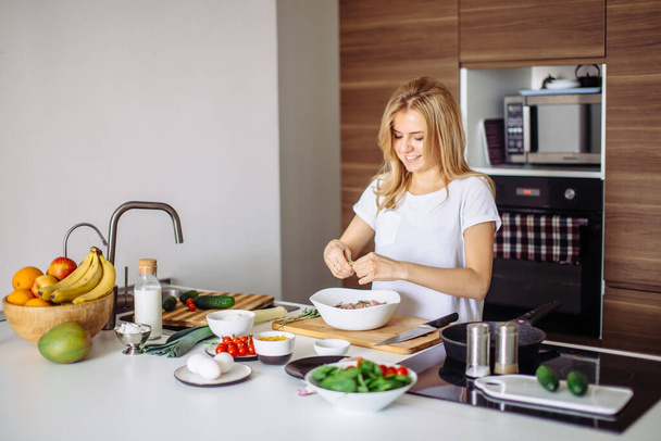 Portrait of happy female wife in white t-shirt cooking dinner at kitchen - Φωτογραφία, εικόνα