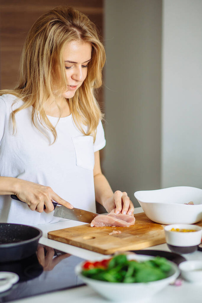 Mujer cortando carne de chiken en una mesa de cocina con un gran cuchillo de chef - Foto, imagen
