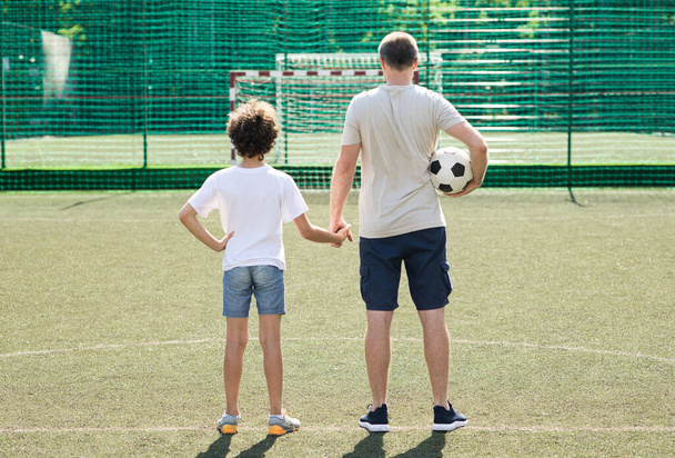 Papa poseren met kleine jongen op voetbalveld, achteraanzicht - Foto, afbeelding