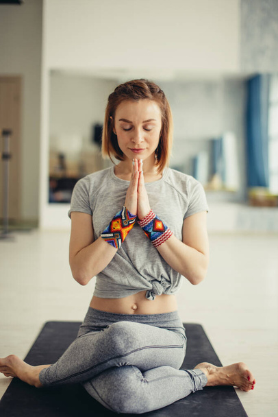 Sporty woman sitting cross-legged in lotus pose in bright room - Photo, image