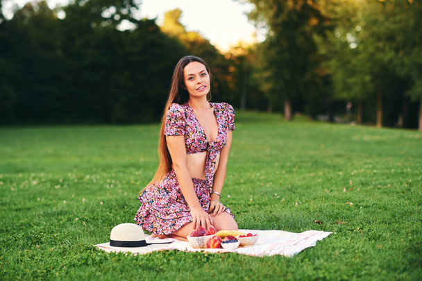 Portrait en plein air de belle jeune femme profitant d'une belle journée dans un parc verdoyant, alimentation saine, collation aux fruits - Photo, image