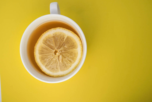 on the yellow background on the left is a white Cup with tea and lemon. - Photo, image