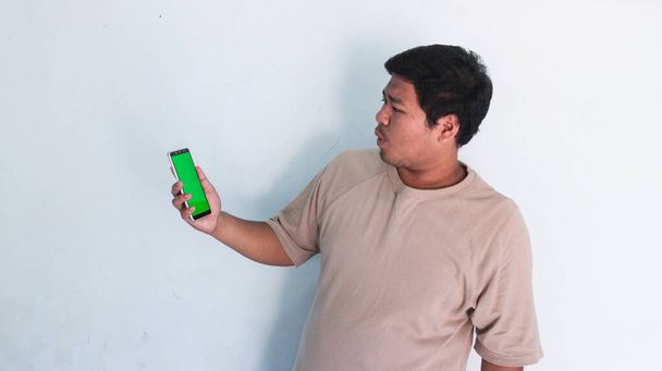 Ασιάτης χοντρός δείχνει το κινητό με την πράσινη οθόνη. - Φωτογραφία, εικόνα