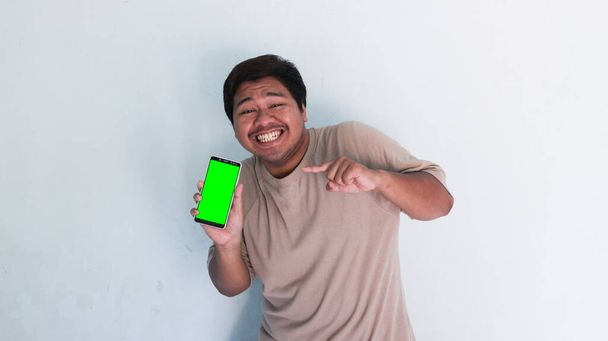 Asian fat man pointing to the cellphone with the green screen - Photo, Image