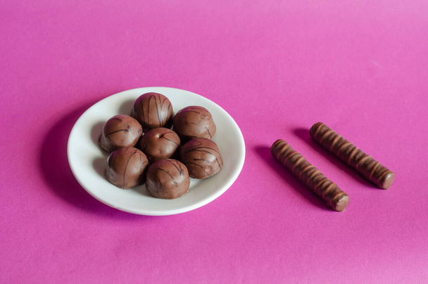 Losowe czekoladki w białym spodku na różowym tle. Porcja różnorodnych wyrobów cukierniczych. Słodkie przekąski. Skupienie selektywne. - Zdjęcie, obraz