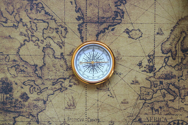 Klasyczny okrągły kompas na tle starej zabytkowej mapy świata jako symbol turystyki z kompasem, podróży z kompasem i zajęć na świeżym powietrzu z kompasem - Zdjęcie, obraz