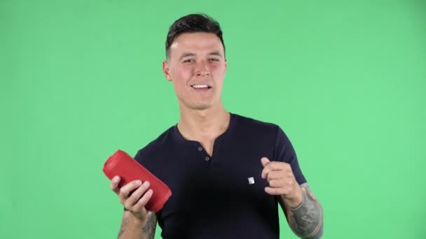 Portrait of a handsome young guy is looking at camera and listening to music with bluetooth portable speaker and dancing. Green screen. - Záběry, video