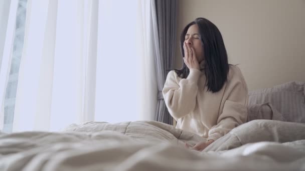 Young adult Asian woman wakes up yawning and Stretch her arm on the bed, lazy morning getting up late on the weekend day off, comfortable bedroom window curtains, natural day light, urban lifestyle  - Footage, Video