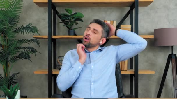 Втомився бізнесмен сидить на стільці в домашньому офісі в бездротових навушниках, роблячи розігрів розтяжок шиї під час болю натирає напружені м'язи після тривалої важкої роботи на комп'ютерному ноутбуці
 - Кадри, відео