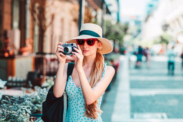 Shot of young female tourist wearing straw hat and sunglasses while taking pictures with her vintage camera.  - Фото, изображение