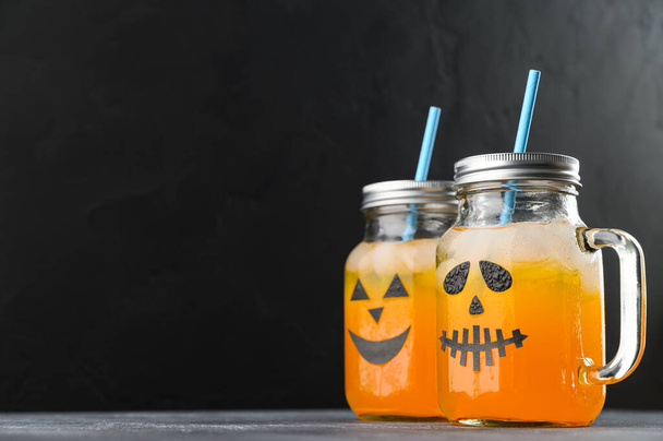 Halloween pumpkin mocktails in glass jars decorated with scary faces on the black background. - Φωτογραφία, εικόνα