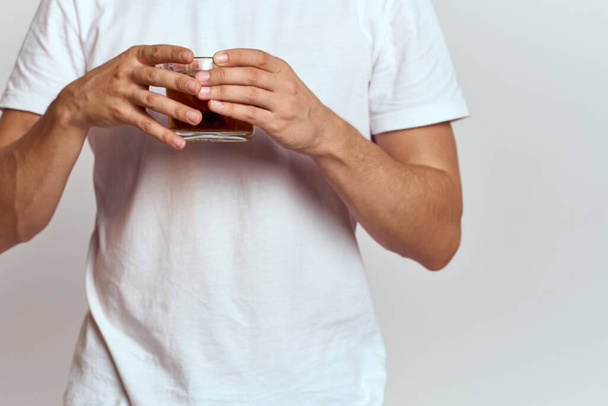 A man with a hot drink of tea in his hands in a white T-shirt on a light background cropped view - Zdjęcie, obraz