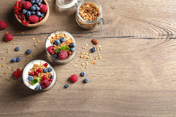 Tasty dessert with yogurt, berries and granola on wooden table, flat lay. Space for text  - Photo, Image