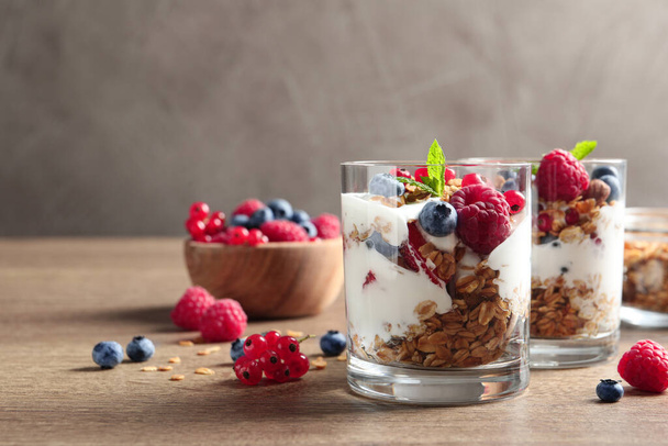 Tasty dessert with yogurt, berries and granola on wooden table, space for text  - Foto, afbeelding