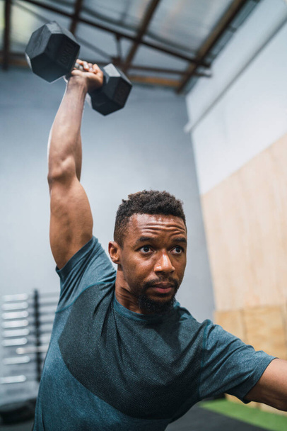 Portrait of young crossfit athlete doing exercise with dumbbell at the gym. Crossfit, sport and healthy lifestyle concept. - 写真・画像