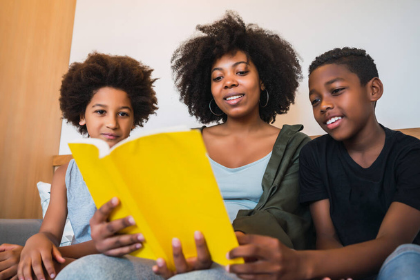 Retrato de la madre afroamericana leyendo un libro a sus hijos en casa. Concepto familia y estilo de vida. - Foto, imagen