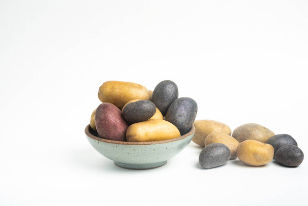Різновид сирої та свіжої картоплі, майстерно розташованої на мисці та столі, встановленому на звичайному білому тлі
. - Фото, зображення