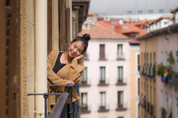 young happy and beautiful Asian Korean woman in hair bun enjoying city view from hotel room balcony in Spain during holidays trip in Europe smiling cheerful in urban background - Photo, image