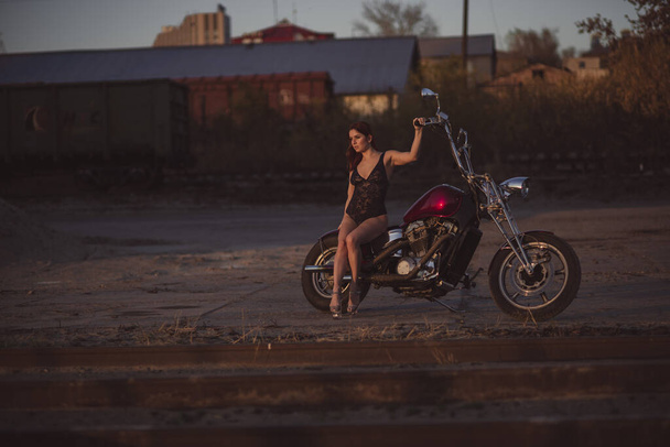 Beautiful sexy woman in lace bodysuit and high heels sits on a motorcycle on an industrial background - Φωτογραφία, εικόνα