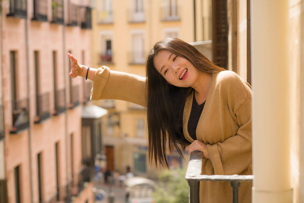young happy and beautiful Asian Chinese woman enjoying city view from hotel room balcony in Spain during holidays trip in Europe smiling cheerful in urban background - 写真・画像