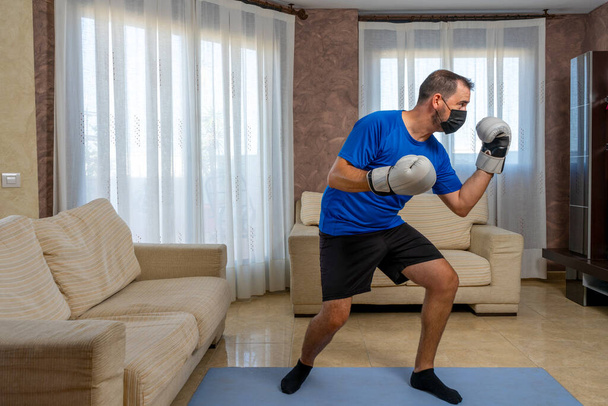 Sedící vousatý muž v černém a modrém sportovním oblečení praktikující bojová umění ve svém obýváku. Koncept cvičení - Fotografie, Obrázek