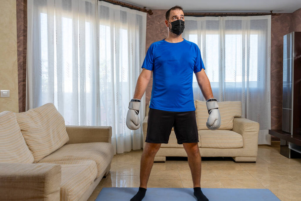 Fit bearded man dressed in black and blue sportswear practicing martial arts in his living room. Exercise concept - Fotoğraf, Görsel