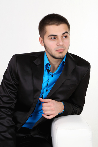 Handsome young man sitting on sofa on light background - Foto, afbeelding