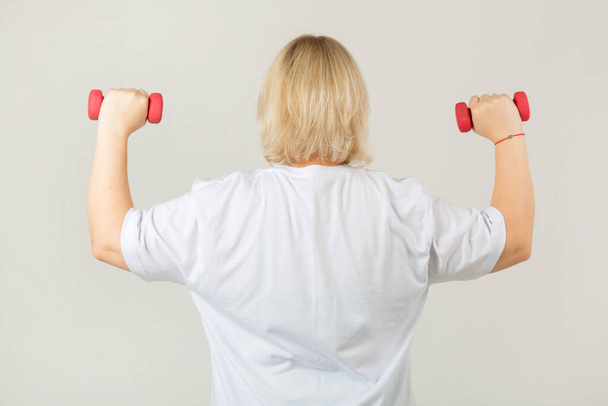 beautiful young plump woman in a white t-shirt on a white background with dumbbells - Φωτογραφία, εικόνα