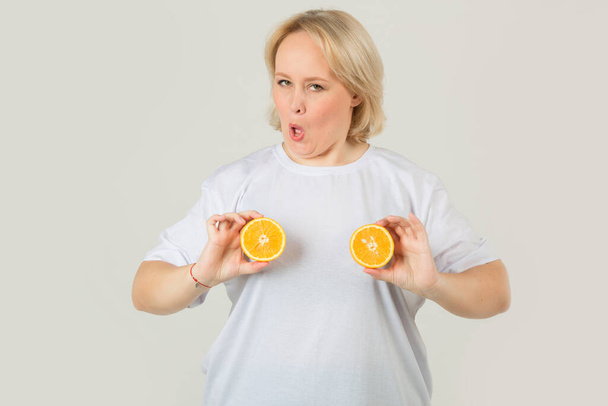 beautiful young plump woman in a white t-shirt on a white background with an orange - Foto, Imagen