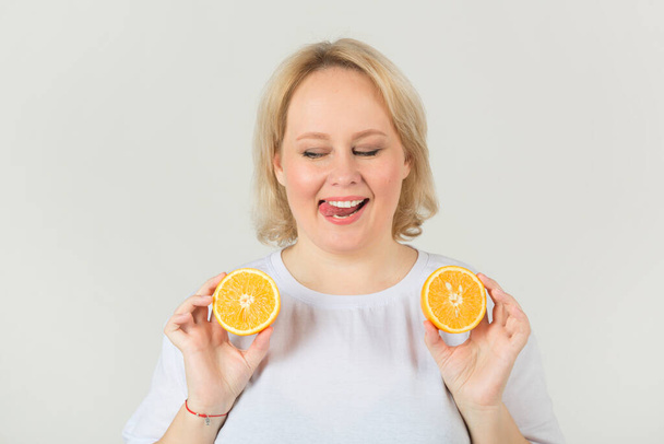 beautiful young plump woman in a white t-shirt on a white background with an orange - Фото, зображення