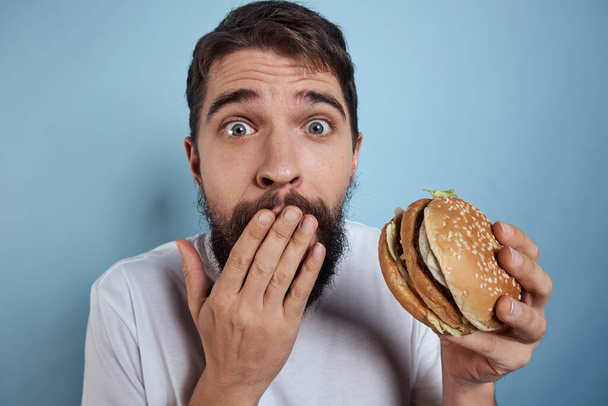 Emotional man hamburger fast food diet food close-up blue background - Valokuva, kuva
