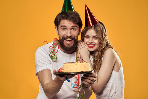 Man and woman birthday festive cake yellow background and caps on the headv - Photo, Image