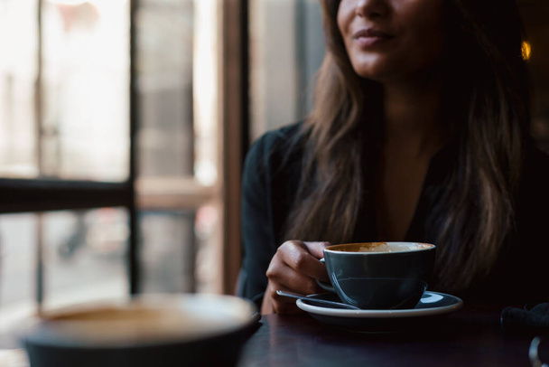 Молодая девушка смешанной расы сидит за столом с кофе  - Фото, изображение