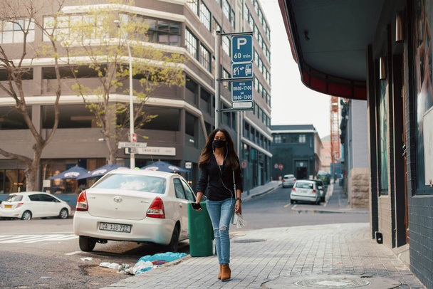Mujer joven con mascarilla en la calle de la ciudad escuchando música  - Foto, imagen